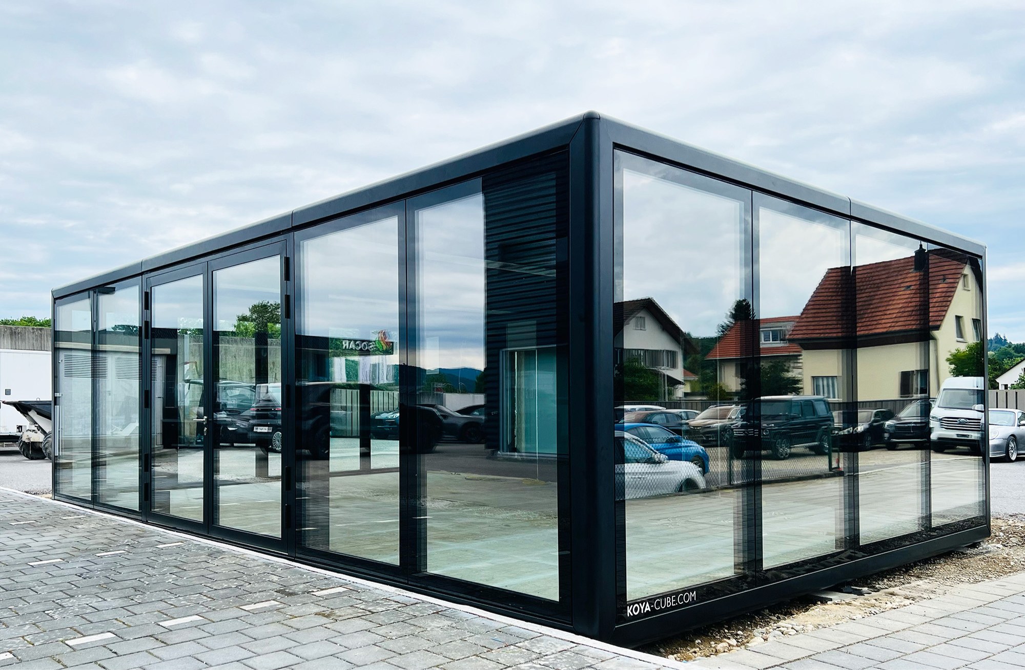KOYA Modul mit raumhoher Verglasung auf einem gepflasterten Platz am Porsche Zentrum Aargau in der Schweiz